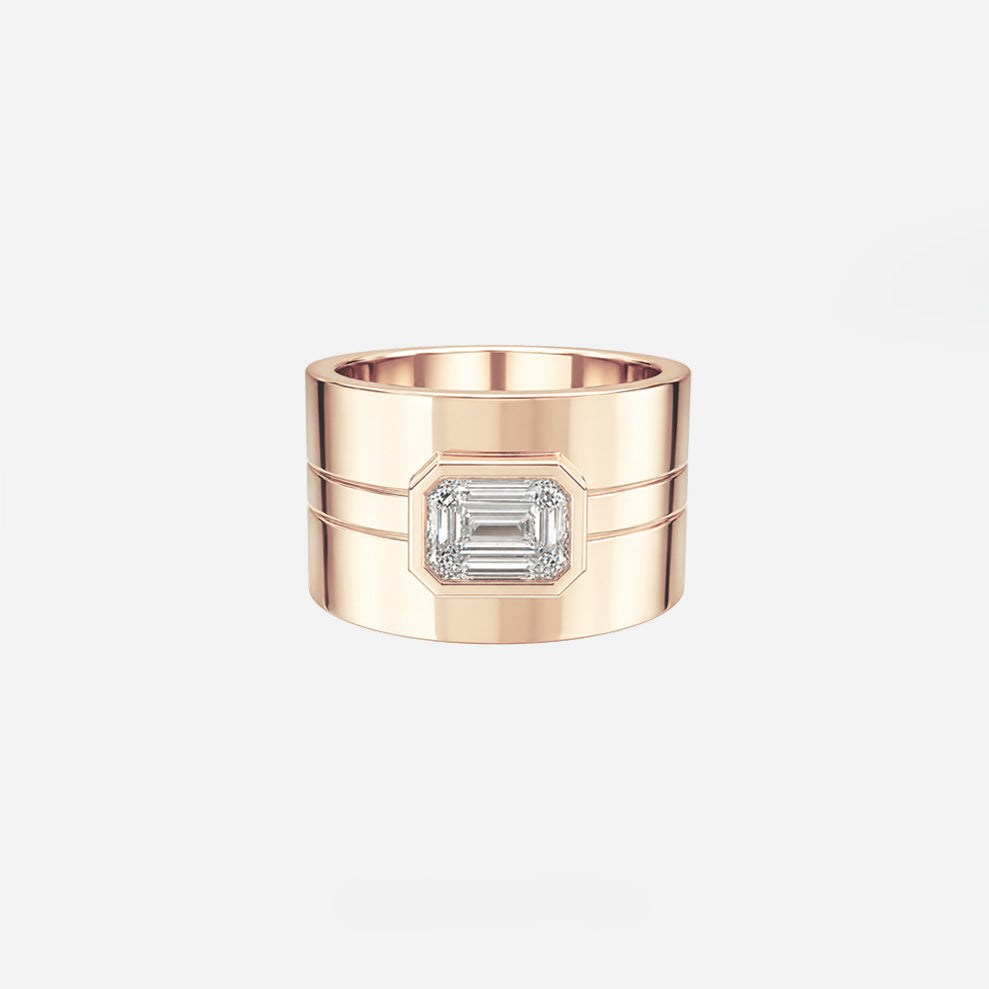 A rose gold ring with a wide band, featuring two horizontal grooves and a central rectangular emerald-cut clear gemstone, shown on a light gray background with small text below.