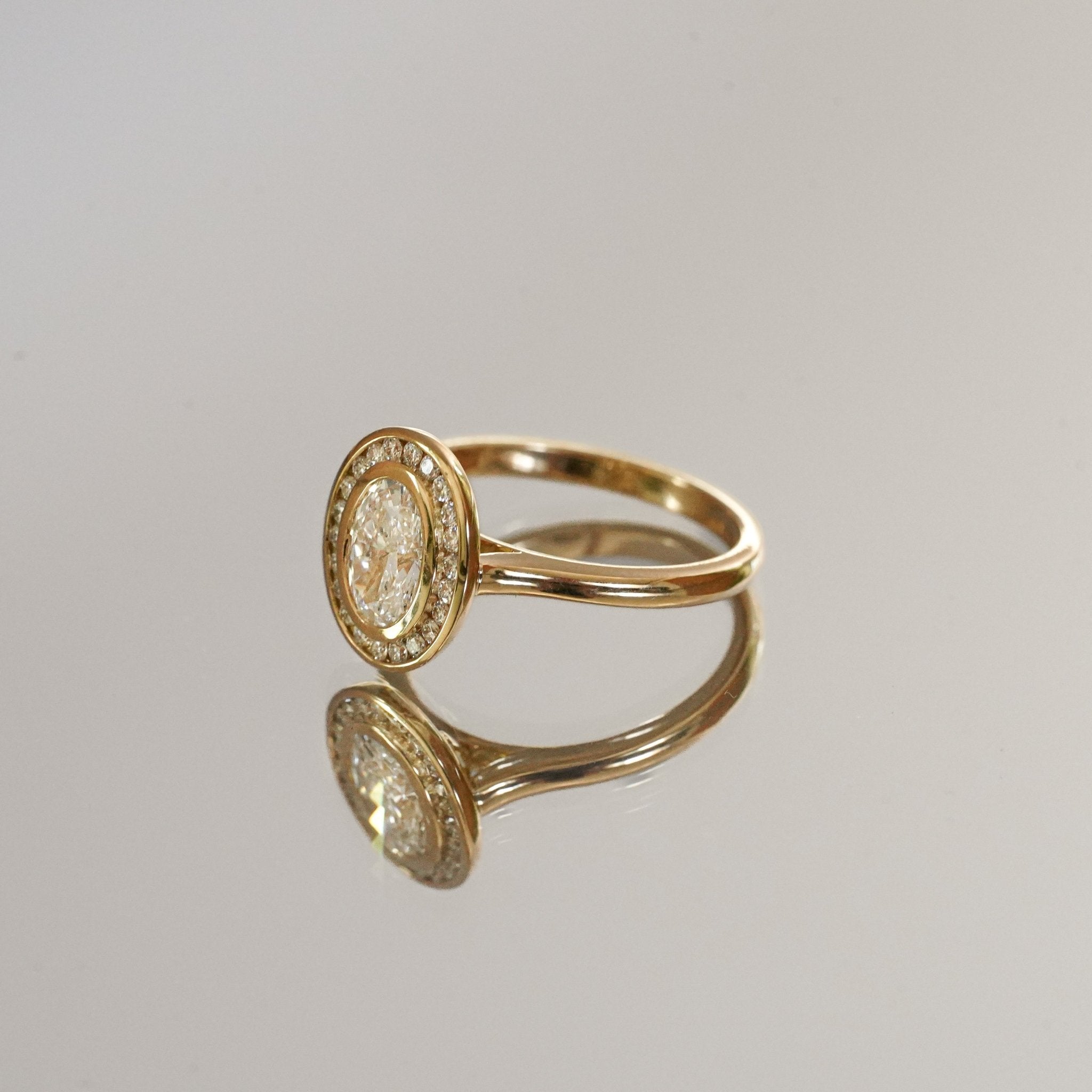 Rings-The Georgia engagement ring showcases a stunning oval diamond in a sleek bezel setting, surrounded by a halo of channel set diamonds. Crafted with a comfort fit band, this design combines clean lines with understated brilliance. Its timeless elegance makes it a sophisticated choice for those seeking a modern yet classic look.-ELIISE MAAR JEWELLERY