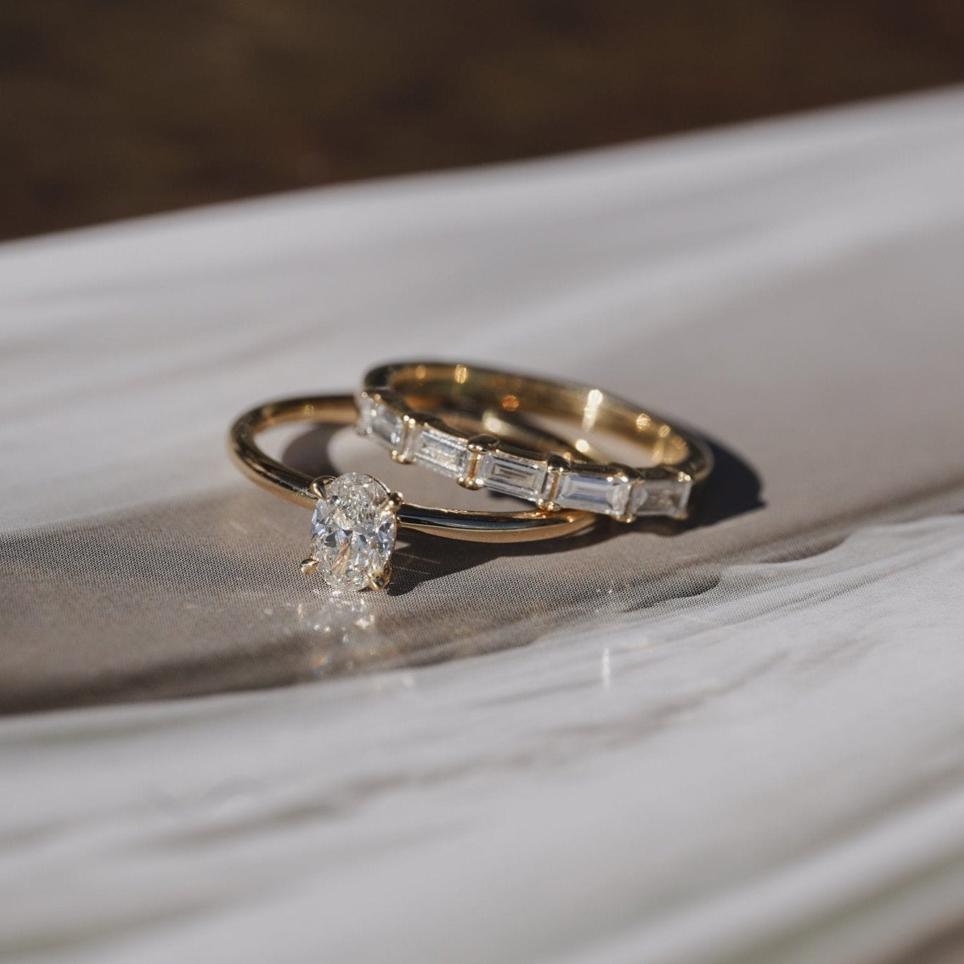 Two gold wedding rings, one with a round-cut diamond and the other with baguette-cut diamonds, resting on a white marble surface.