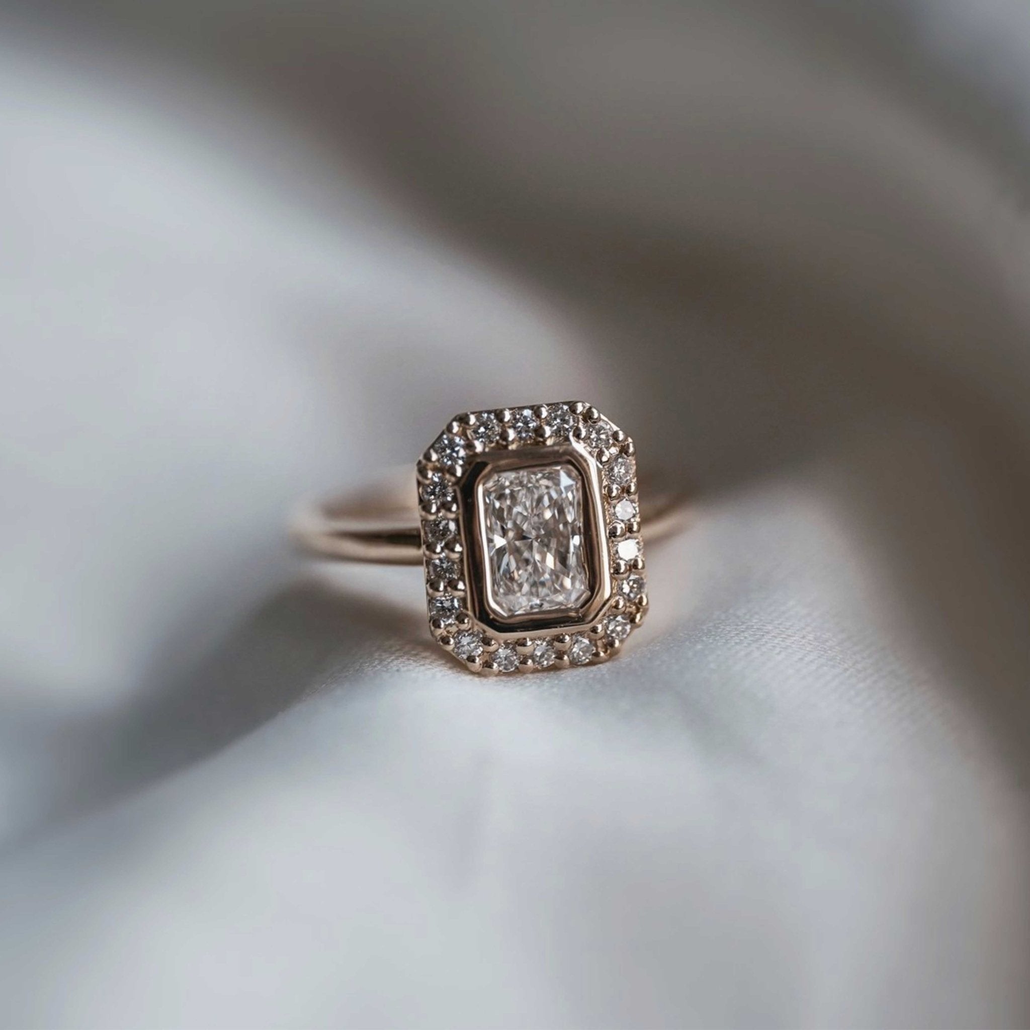 Rings-A contemporary take on an art-deco design. The Holly boasts a stunning bezel set radiant cut centre diamond adorned by a striking halo. This ring uses and enhances the metal in which the stones are set in to create a design that is powerful and elegant.-ELIISE MAAR JEWELLERY