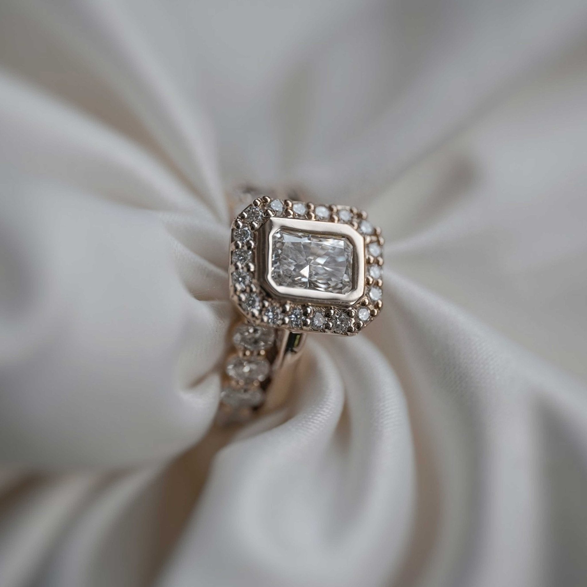 Rings-A contemporary take on an art-deco design. The Holly boasts a stunning bezel set radiant cut centre diamond adorned by a striking halo. This ring uses and enhances the metal in which the stones are set in to create a design that is powerful and elegant.-ELIISE MAAR JEWELLERY