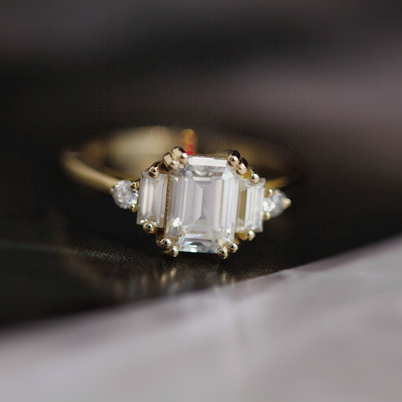 Rings-Product Details - Features an 7 x 5mm emerald cut Supernova Moissanite as the centre stone and baguette and round on the sides- Moissanite is a laboratory created gemstone that is very durable making it suitable for an engagement ring and everyday wear. Moissanite is not a lab grown diamond. The ring will come with a card of authenticity stating that it is featuring a Supernova Moissanite.- The ring is 1.80mm wide and thick-ELIISE MAAR JEWELLERY