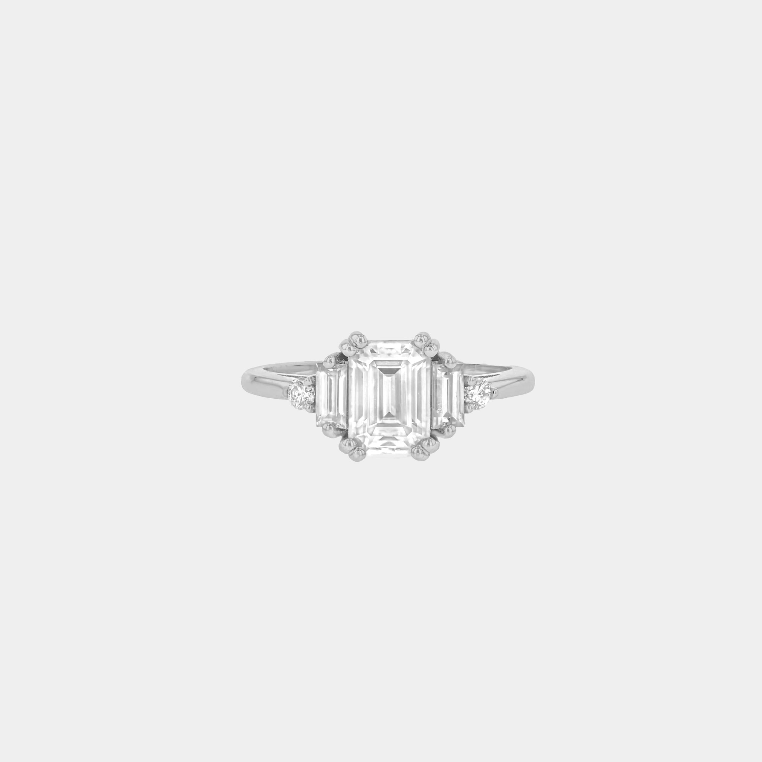 Rings-Product Details - Features an 7 x 5mm emerald cut Supernova Moissanite as the centre stone and baguette and round on the sides- Moissanite is a laboratory created gemstone that is very durable making it suitable for an engagement ring and everyday wear. Moissanite is not a lab grown diamond. The ring will come with a card of authenticity stating that it is featuring a Supernova Moissanite.- The ring is 1.80mm wide and thick-ELIISE MAAR JEWELLERY