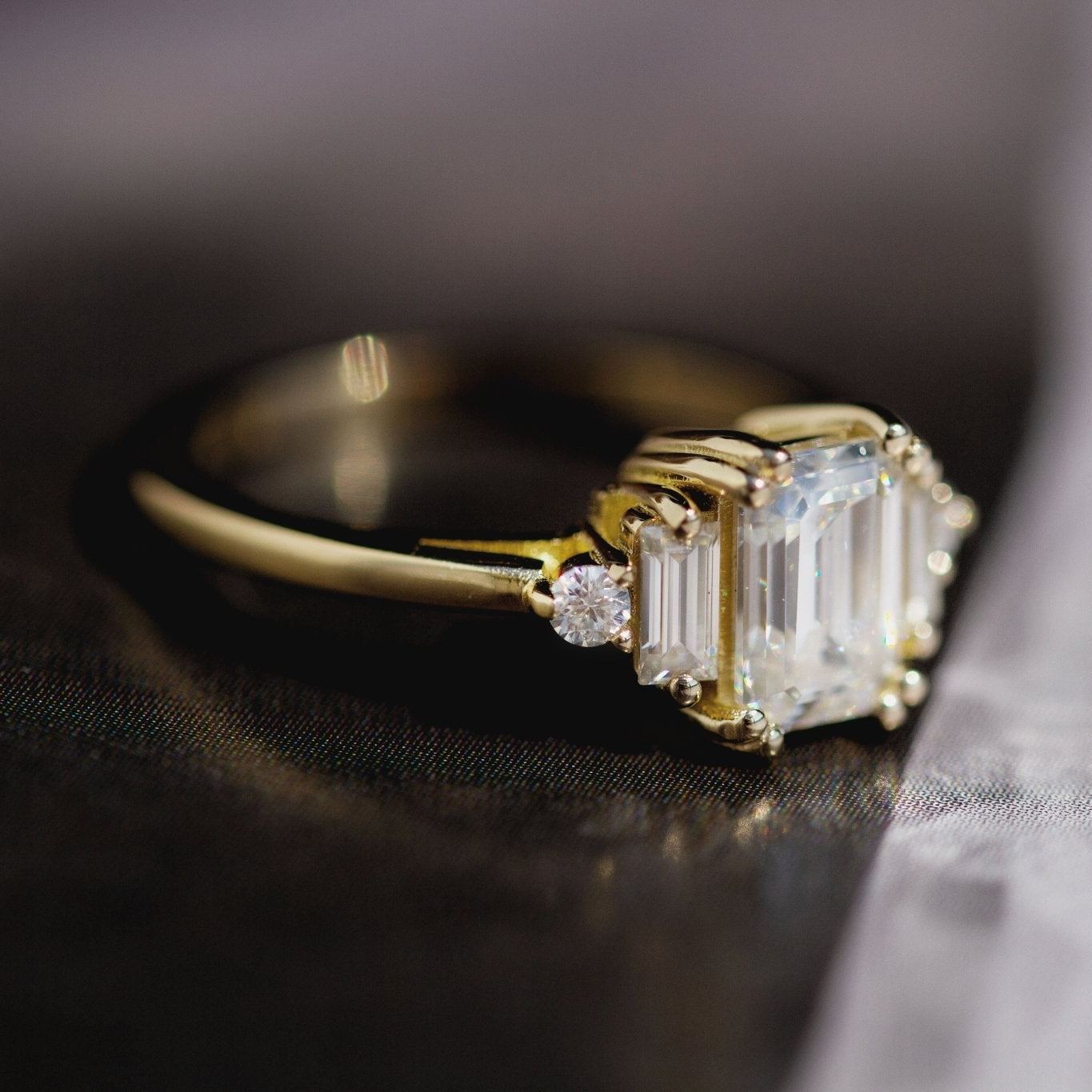 Rings-Product Details - Features an 7 x 5mm emerald cut Supernova Moissanite as the centre stone and baguette and round on the sides- Moissanite is a laboratory created gemstone that is very durable making it suitable for an engagement ring and everyday wear. Moissanite is not a lab grown diamond. The ring will come with a card of authenticity stating that it is featuring a Supernova Moissanite.- The ring is 1.80mm wide and thick-ELIISE MAAR JEWELLERY