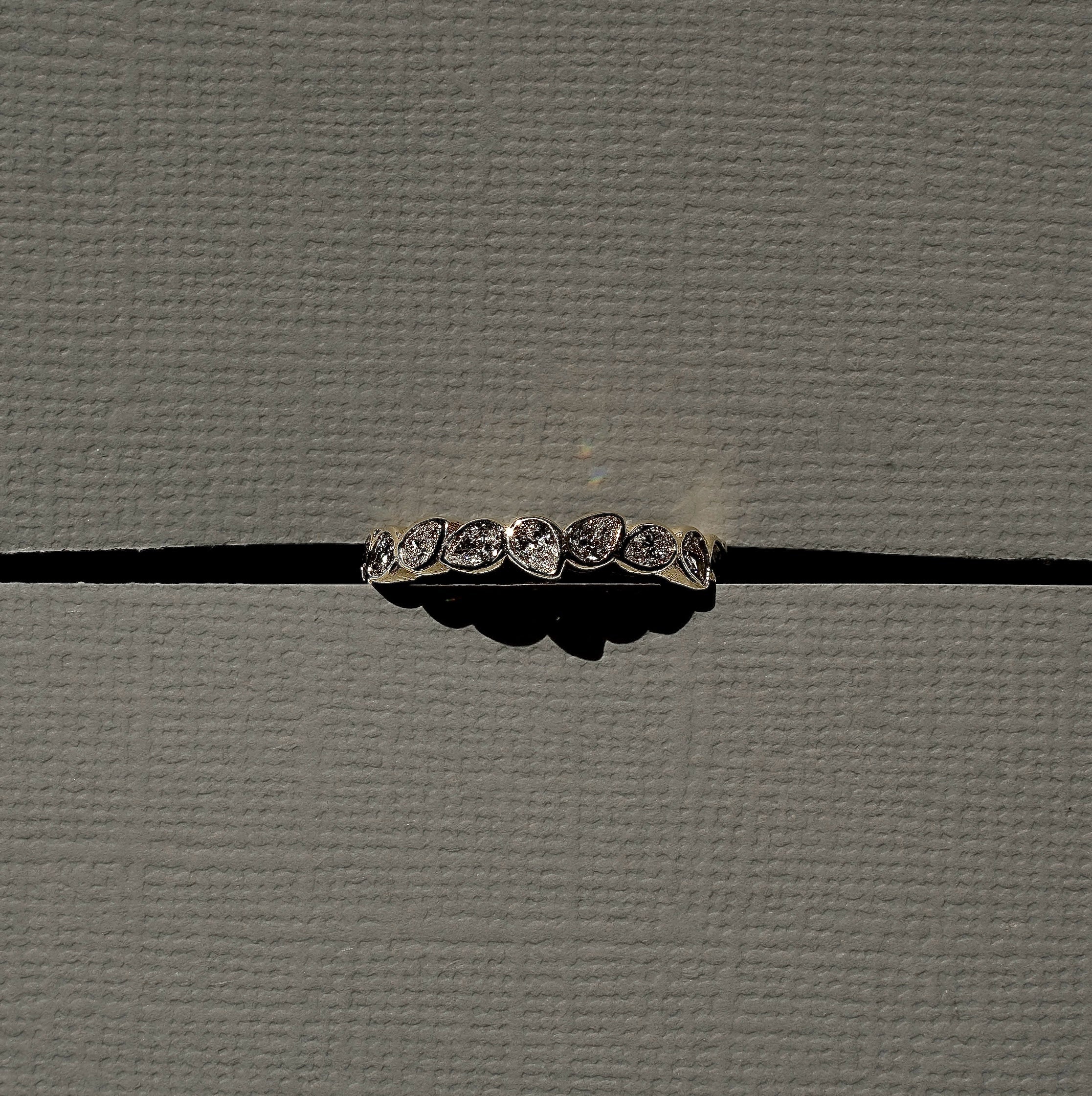 A silver-toned band ring with five round-cut clear gemstones, photographed horizontally against a textured gray background with a black horizontal line behind it.
