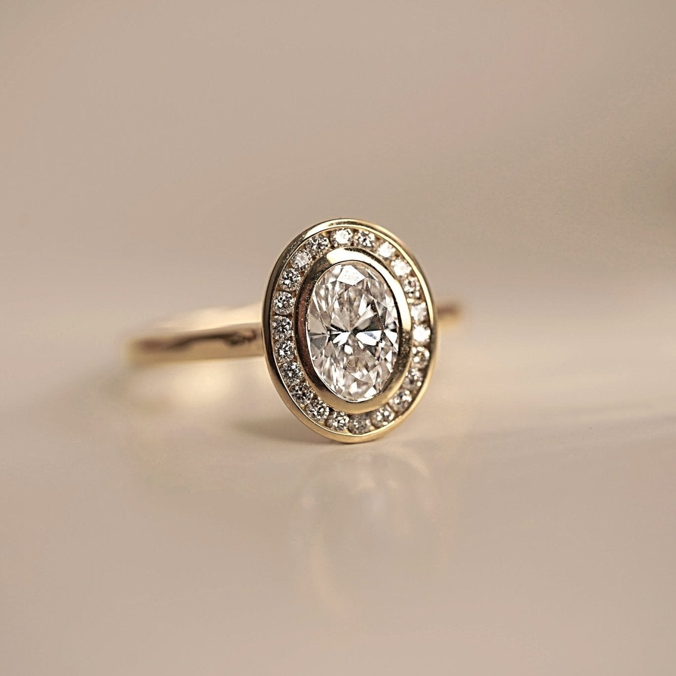 Rings-The Georgia engagement ring showcases a stunning oval diamond in a sleek bezel setting, surrounded by a halo of channel set diamonds. Crafted with a comfort fit band, this design combines clean lines with understated brilliance. Its timeless elegance makes it a sophisticated choice for those seeking a modern yet classic look.-ELIISE MAAR JEWELLERY