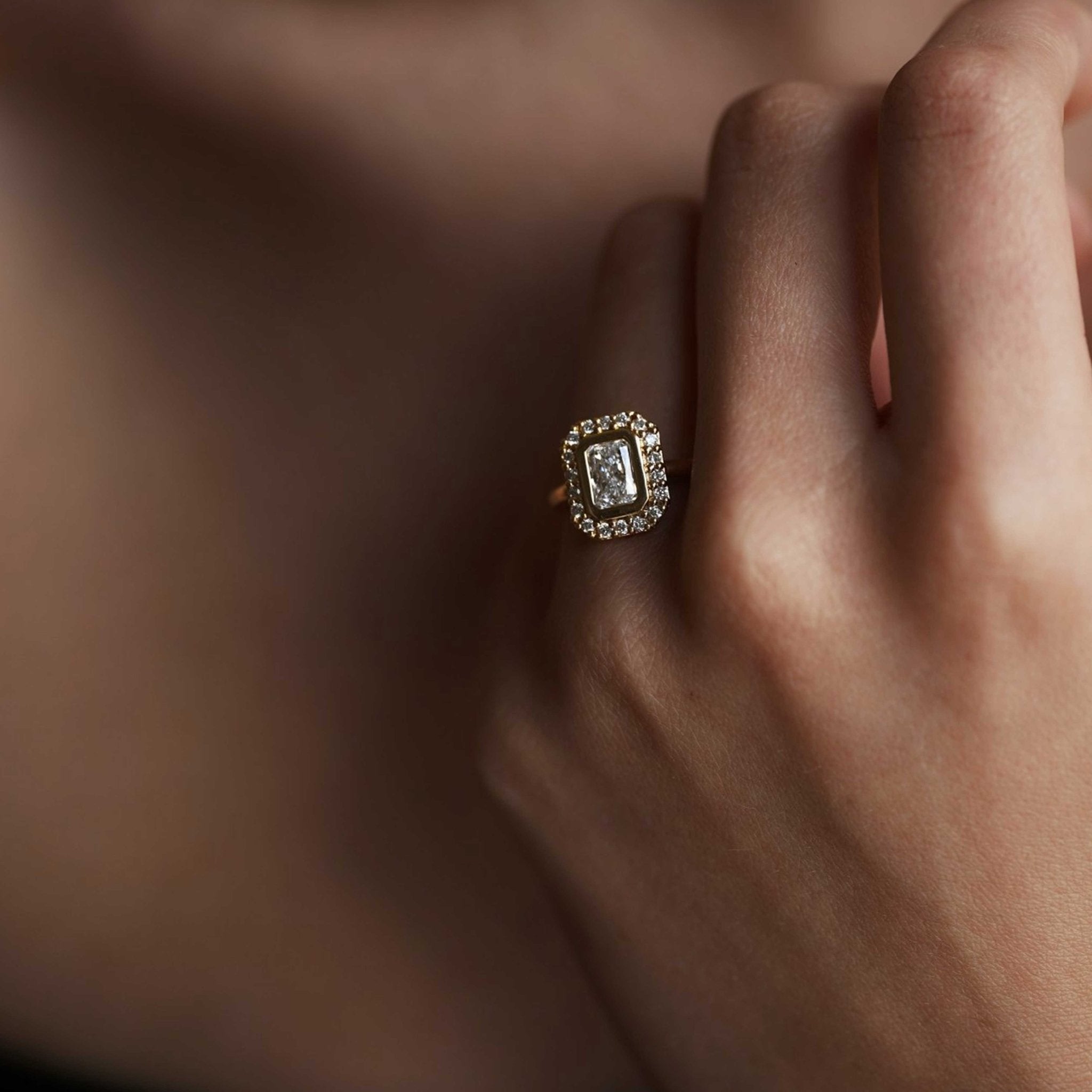 Rings-A contemporary take on an art-deco design. The Holly boasts a stunning bezel set radiant cut centre diamond adorned by a striking halo. This ring uses and enhances the metal in which the stones are set in to create a design that is powerful and elegant.-ELIISE MAAR JEWELLERY