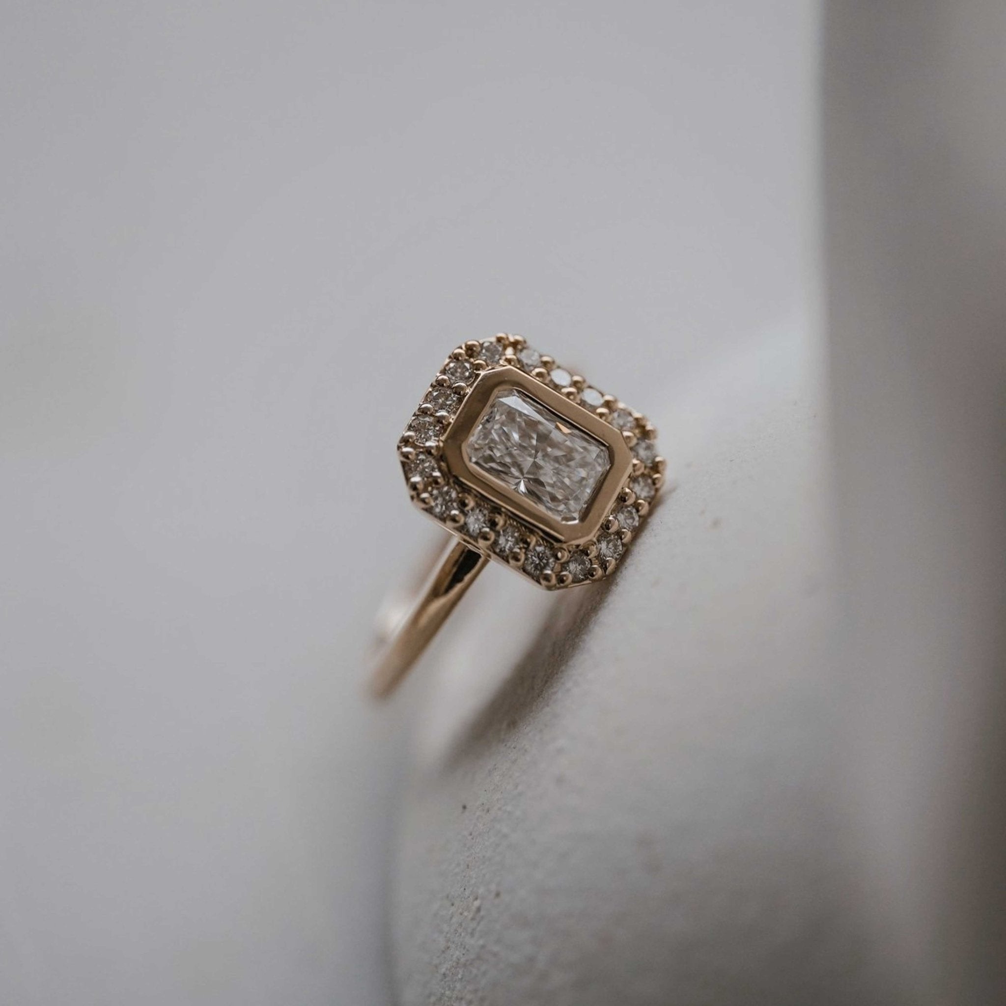 Rings-A contemporary take on an art-deco design. The Holly boasts a stunning bezel set radiant cut centre diamond adorned by a striking halo. This ring uses and enhances the metal in which the stones are set in to create a design that is powerful and elegant.-ELIISE MAAR JEWELLERY